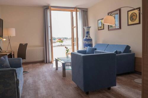 Eine Sitzlounge in einem der Kastaniehof Zimmer mit blauer Couch und blauem Sessel, dahinter eine geöffnete Terrassentür.
