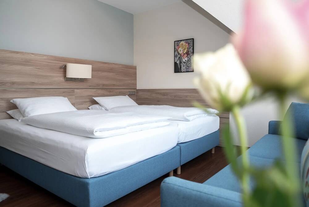 Ein Doppelzimmer mit Bett und unscharfer Blumen-Deko im Vordergrund im Messe Hotel Erding.