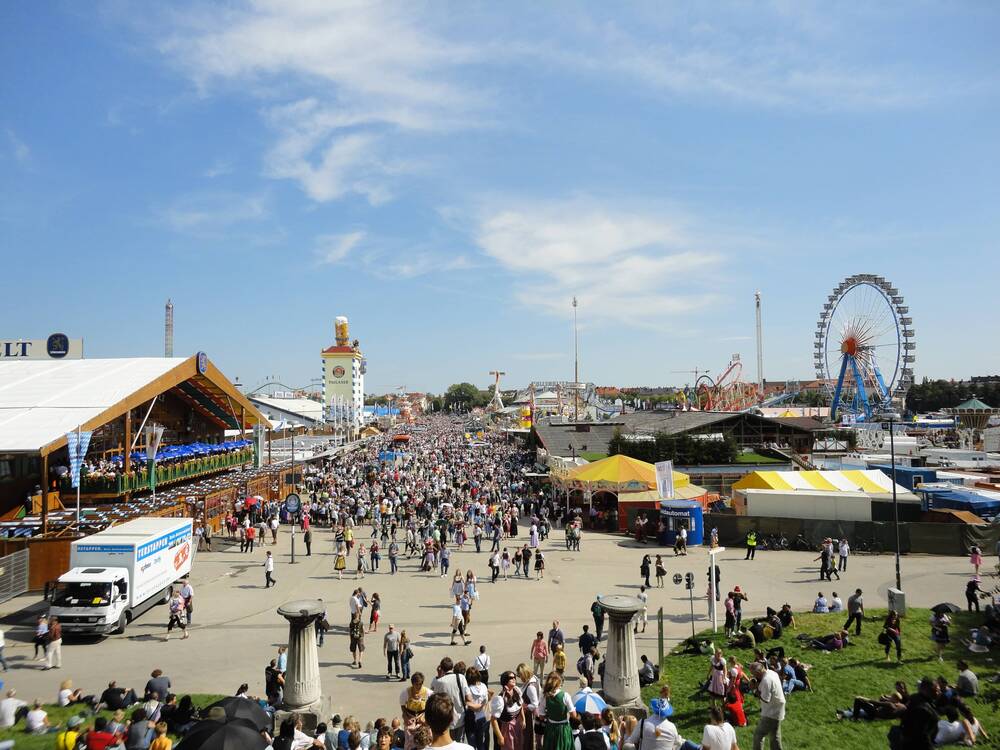 Das Oktoberfest München auf der Theresienwiese mit zahlreichen Besuchern, großen Festzelten, Fahrgeschäften wie dem Riesenrad und typischer Wiesn-Atmosphäre. Perfekt für alle, die ein Oktoberfest Hotel in Erding suchen.
